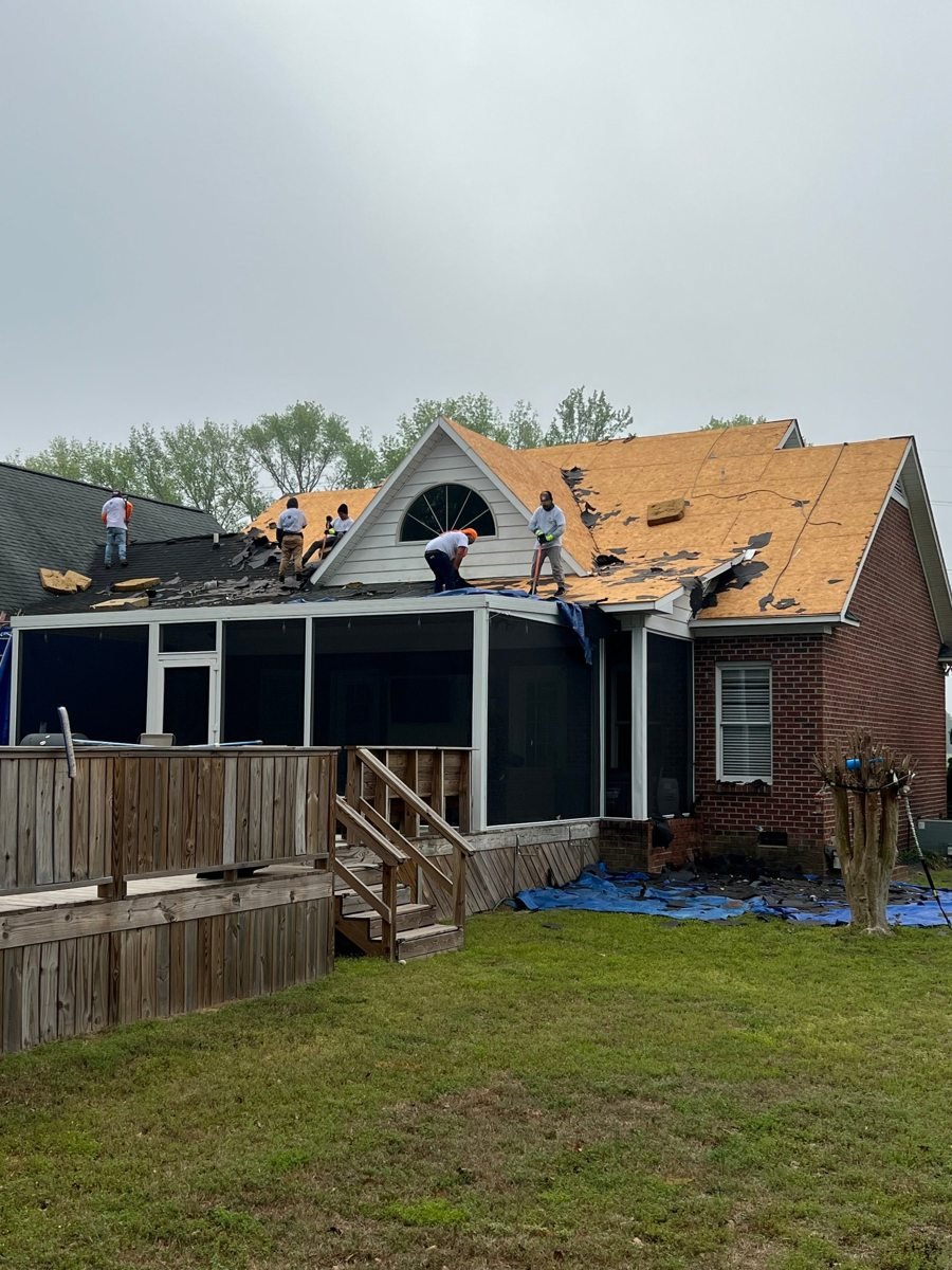 Roofers working on a brick home above a screened porch