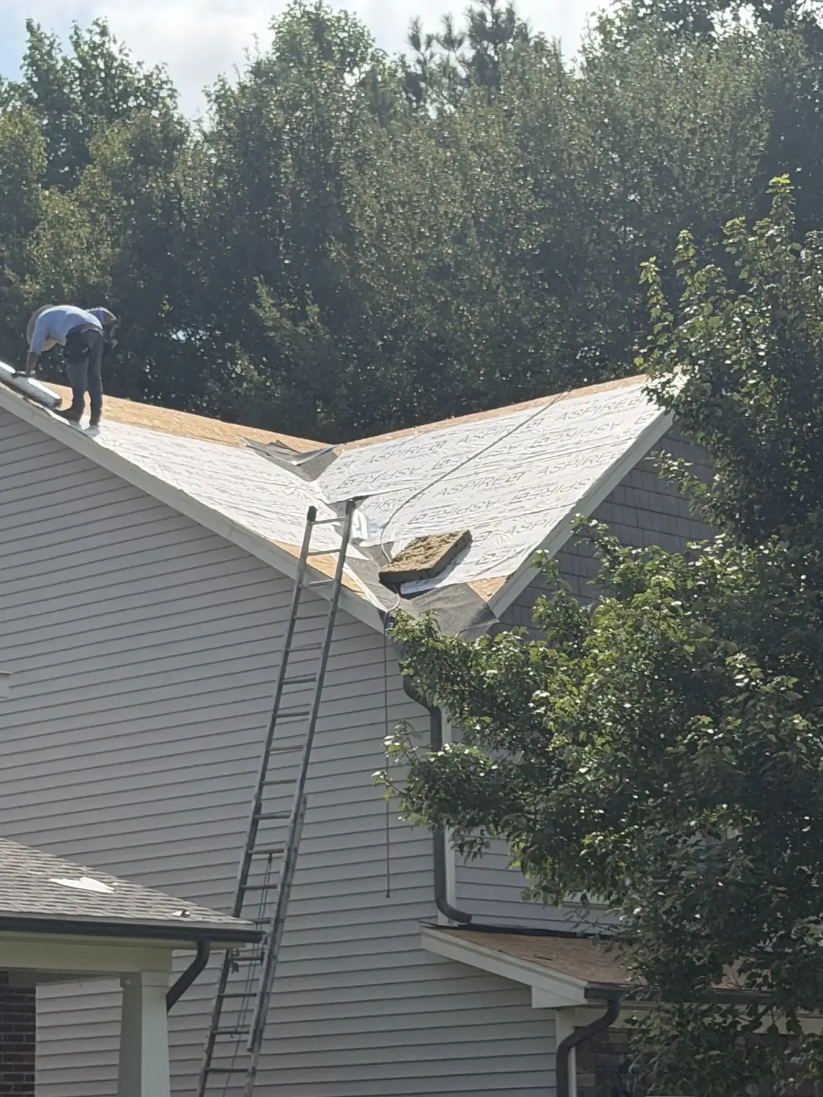 Gray siding, gable and gutters on a two-story home with a roofer on the roof