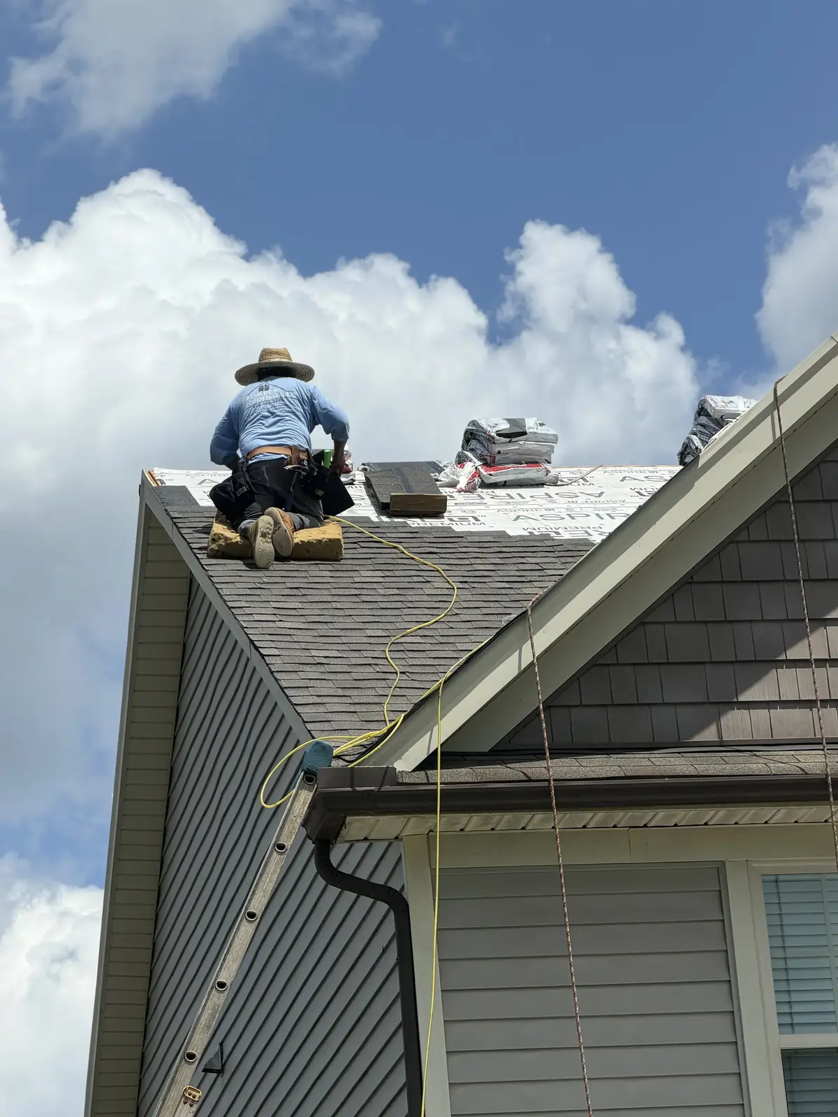Salvation Roofing roofer working at a gable above gray siding
