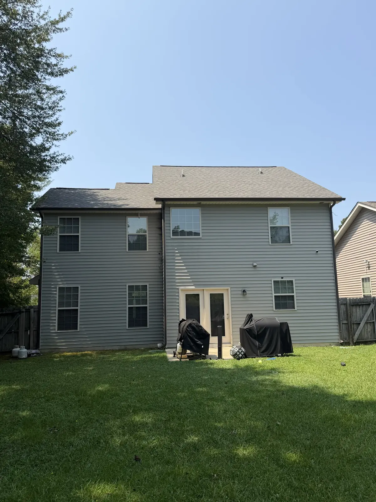 Back of a two-story home with gray siding and a patio