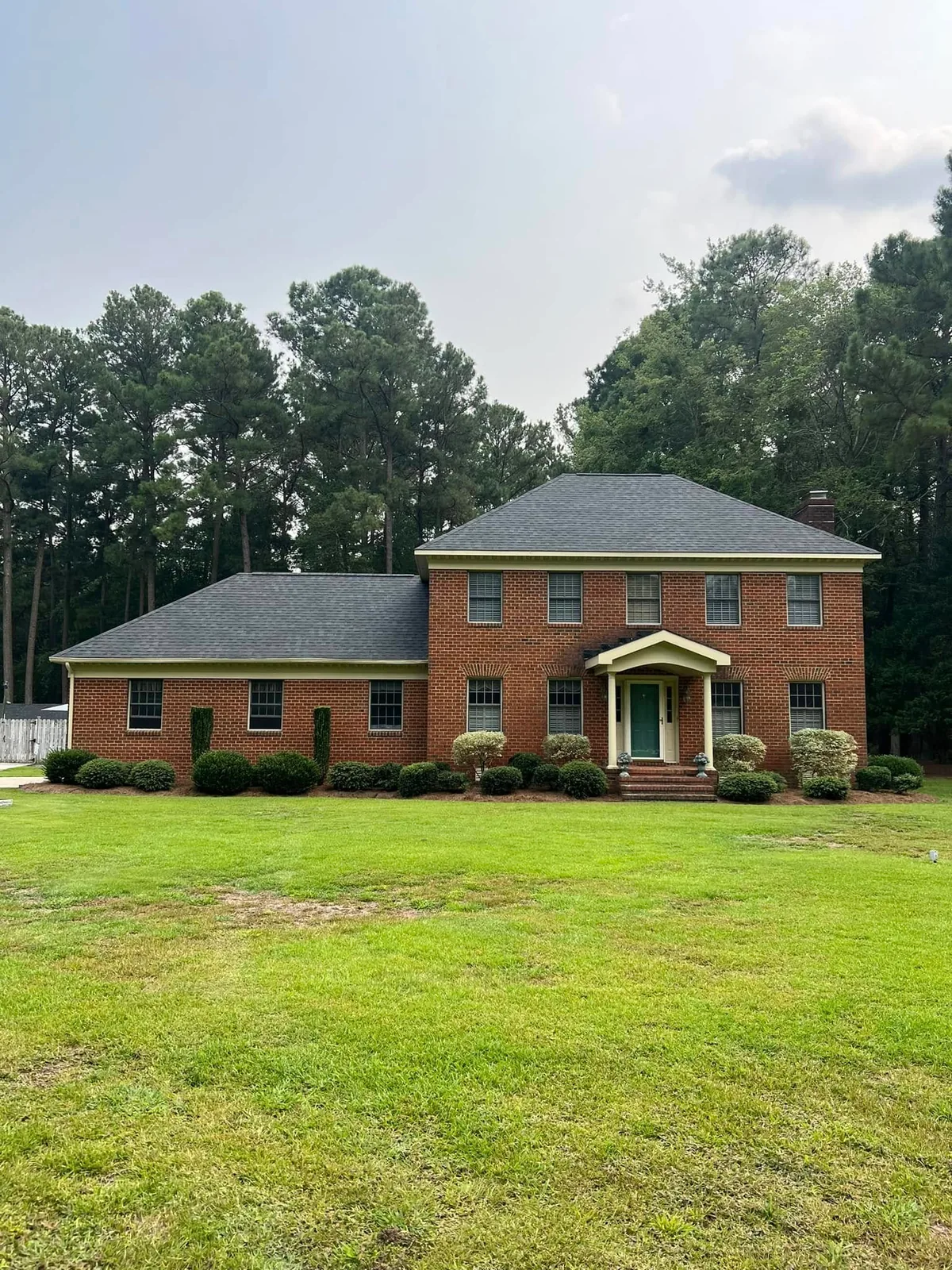 Brick two-story home with a shingle roof and large front lawn